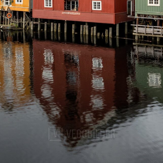 Fargerike trebygninger langs Nidelva i Trondheim på en overskyet dag, med speilblankt vann som gir en vakker refleksjon., fotokunst veggbilde / plakat av Eirik Sørstrømmen