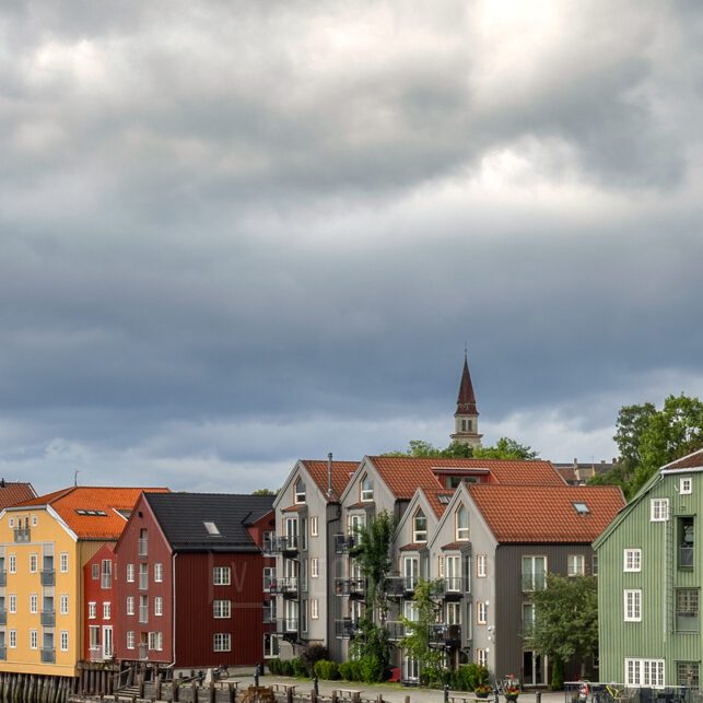 Fargerike trebygninger langs Nidelva i Trondheim på en overskyet dag, med speilblankt vann som gir en vakker refleksjon., fotokunst veggbilde / plakat av Eirik Sørstrømmen